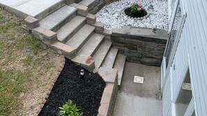 A landscaped garden with a stone staircase leading to a circular seating area, surrounded by mulch and small plants. - Charming, spacious, exceptionally clean & private apt! Ideal Ithaca location! (Ithaca)