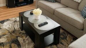A living room with a sofa, a coffee table with a vase and remote, a TV, and a wall clock. - Charming, spacious, exceptionally clean & private apt! Ideal Ithaca location! (Ithaca)