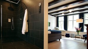 A modern bathroom with dark tiles, a shower, and a white towel hanging on the wall. - 1637 Historic Canal View Suites (Amsterdam)