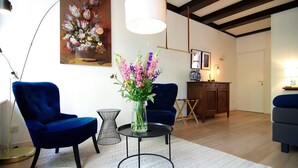 A modern living room with two blue armchairs, a round coffee table with a vase of flowers, and a painting on the wall. - 1637 Historic Canal View Suites (Amsterdam)
