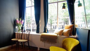 A room with a window seat, wooden chairs, a yellow armchair, and a vase with flowers. - 1637 Historic Canal View Suites (Amsterdam)