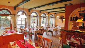 A restaurant with multiple tables, wooden chairs, and large windows with curtains.