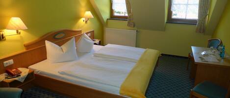 A hotel room with a large bed, two bedside lamps, a desk with a chair, and a window with curtains.