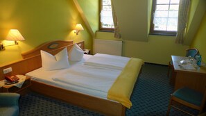 Habitación de hotel con una cama grande, dos lámparas de noche, un escritorio con una silla y una ventana con cortinas.