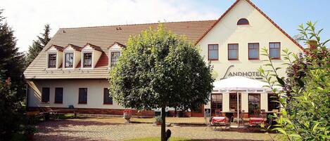 A traditional building with a tiled roof, a central tree, and outdoor seating for a restaurant.