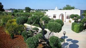 A building with a white facade and arched windows, surrounded by well-maintained greenery and a clear sky.