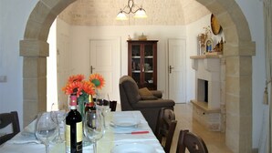 A dining area with a stone archway, a chandelier, a dining table set with plates and wine glasses, and a sofa in the background.