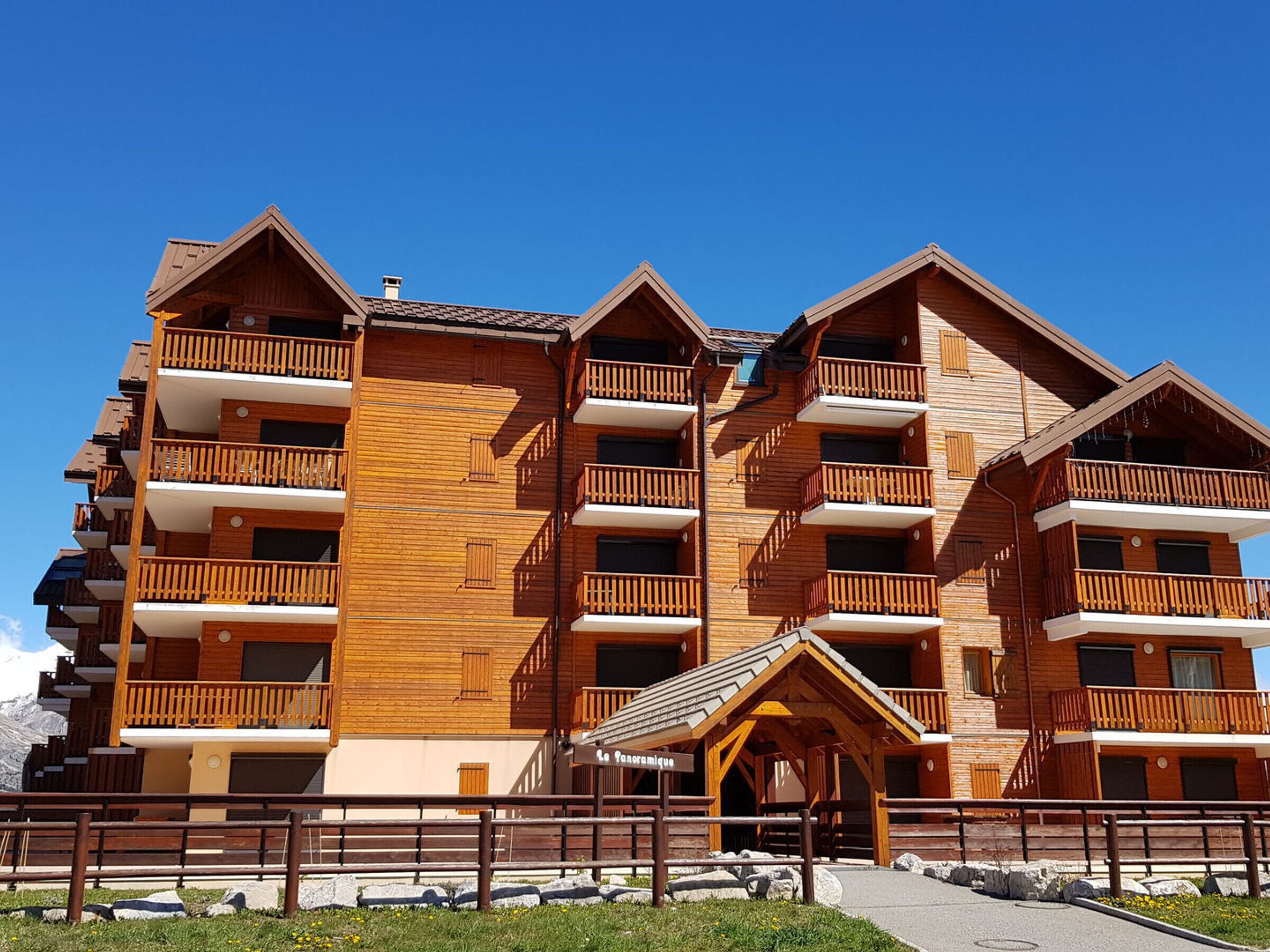 A multi-story wooden building with balconies, a covered entrance, and a clear sky.