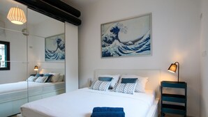 A hotel room with a large bed, a bedside table, a lamp, and a wall painting. - MAMAD Trendy Apt & Balcony on Sheinkin Street by FeelHome (Tel Aviv - Jaffa)