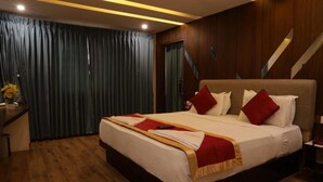 Quarto de hotel com uma cama grande, piso de madeira, uma mesa com um vaso de flores e vista para uma escadaria.