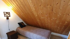 A small, cozy room with a sloped ceiling, a single bed, a bedside table, and a chair. - Semi-Detached Chalet, 3 Rooms, 7 Pers, Terrace, Free Parking, Pets Allowed (La Joue du Loup)