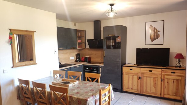 A compact kitchen with a dining area, wooden cabinets, a refrigerator, a microwave, and a television. - Semi-Detached Chalet, 3 Rooms, 7 Pers, Terrace, Free Parking, Pets Allowed (La Joue du Loup)
