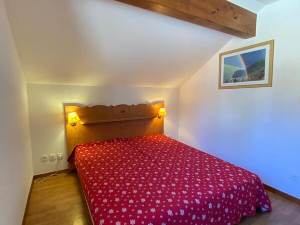A bedroom with a wooden headboard, a red bedspread, and a framed picture on the wall.