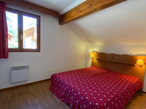 A bedroom with a wooden ceiling, a bed with a red floral bedspread, two wall-mounted lamps, and a window with curtains. - Cozy chalet for 8 with parking at La Joue du Loup (La Joue du Loup)