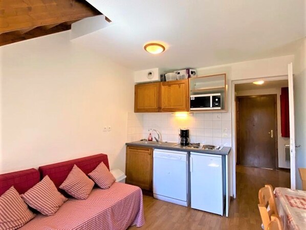 Ett kompakt bostadsutrymme med ett litet kök, en röd soffa och en matplats.