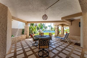 Una zona de estar al aire libre con techo, vistas a la piscina, paredes de piedra y suelo con diseño.