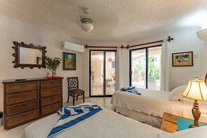 Une chambre d’hôtel avec deux lits, une commode, une chaise, un ventilateur de plafond et une vue sur l’espace extérieur.