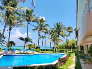 A pool area with lounge chairs and palm trees, overlooking a clear blue sky and ocean. - Charming, cozy beachfront condo in South Akumal, pool, AC and WiFi! (South Akumal)
