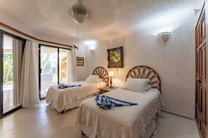 A room with two beds, a ceiling fan, a painting, and a door. - Charming, cozy beachfront condo in South Akumal, pool, AC and WiFi! (South Akumal)