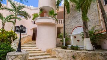 A building with a stone facade, a set of stairs leading to a balcony, and palm trees.
