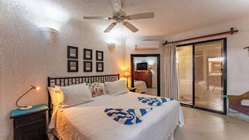 Quarto de hotel com cama, mesa de cabeceira, ventilador de teto, televisão e porta de vidro deslizante para uma varanda.