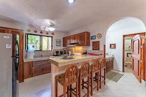 A kitchen with wooden cabinets, a marble countertop, and a built-in bar area with bar stools.