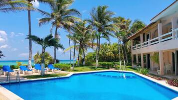 A swimming pool with blue water, surrounded by palm trees and a building with a balcony.