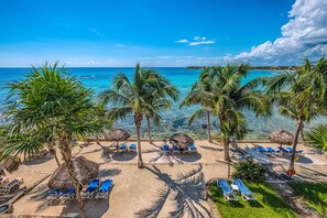 A beach with clear blue water, palm trees, and lounge chairs. - Beachfront Penthouse with Pool and Caribbean Sea Views (Akumal)