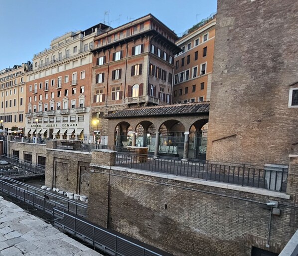 An ancient Roman site with stone ruins, a paved walkway, and a brick building with arched windows.