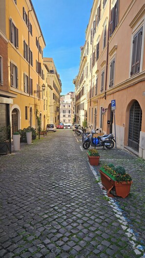 Rua de calçada com edifícios amarelos, scooters estacionados e vasos de plantas.