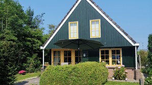 A green house with yellow-framed windows, a chimney, and a well-maintained lawn.