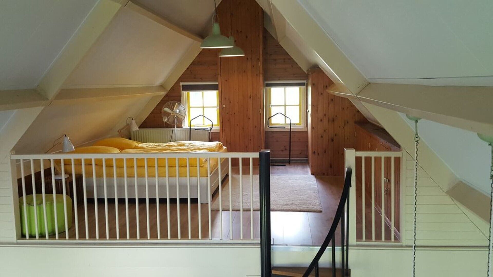 Een slaapkamer op zolder met hoge plafonds, een bed, een ventilator en een raam.