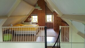 A high-ceilinged attic bedroom with a bed, a fan, and a window.