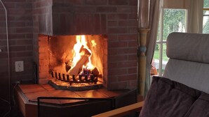 A room with a brick fireplace, a wooden chair, and a window with curtains.