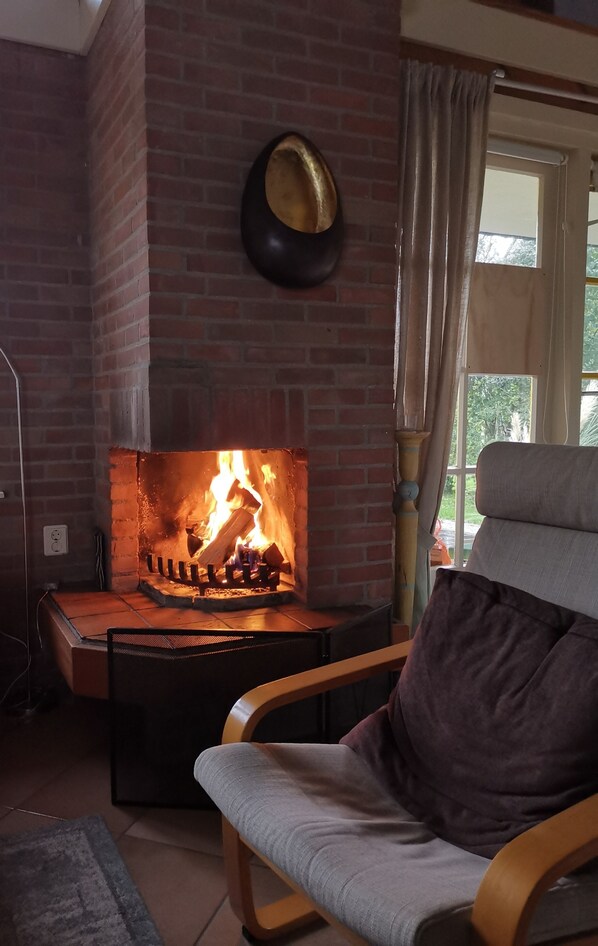 A room with a brick fireplace, a wooden chair, and a window with curtains.