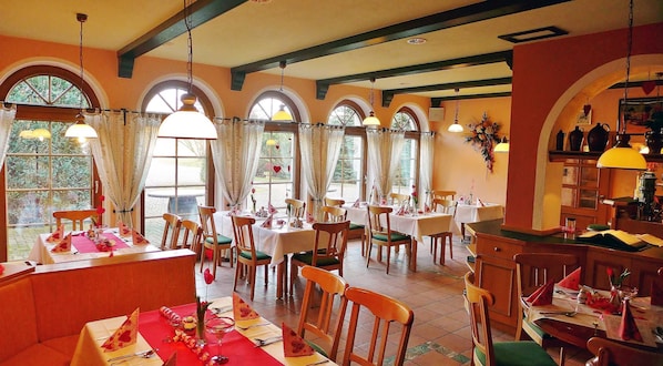 Un restaurant avec de nombreuses tables, des chaises en bois et de grandes fenêtres dotées de rideaux.