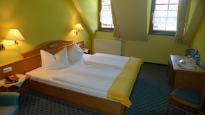 Une chambre d’hôtel avec un grand lit, deux lampes de chevet, un bureau avec une chaise et une fenêtre avec des rideaux.