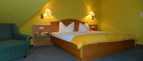 A hotel room with a bed, a nightstand, a lamp, and a chair.