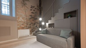 Um interior moderno com um sofá cinza, uma escada e uma parede com padrão de folhas.