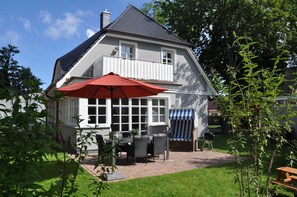 A two-story house with a balcony, a patio with a table and chairs, and a barbecue grill.