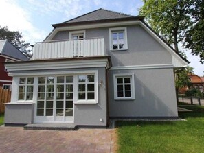 A two-story house with a balcony, large windows, and a paved driveway.