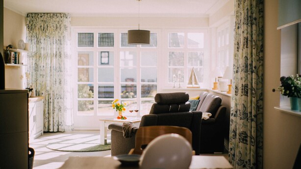 A living room with a sofa, armchair, and a dining table with a vase of flowers. - Haus Fock - HausFock (Prerow)