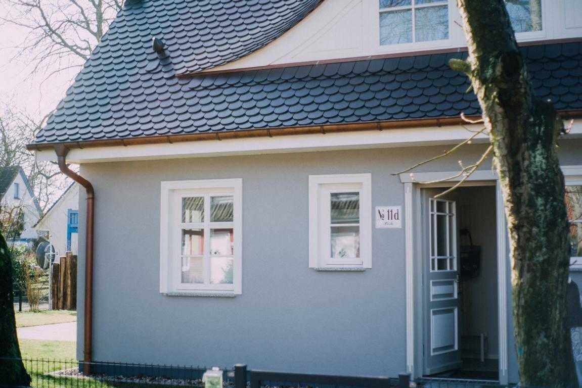 A house with a grey exterior, a tiled roof, and two windows with white frames.