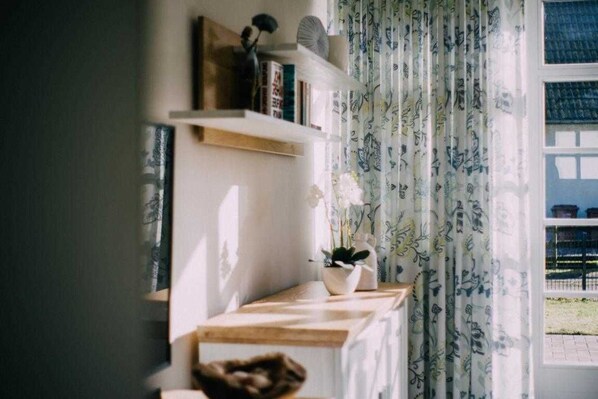 A room with a window, a shelf with books and decorative items, and a potted plant.