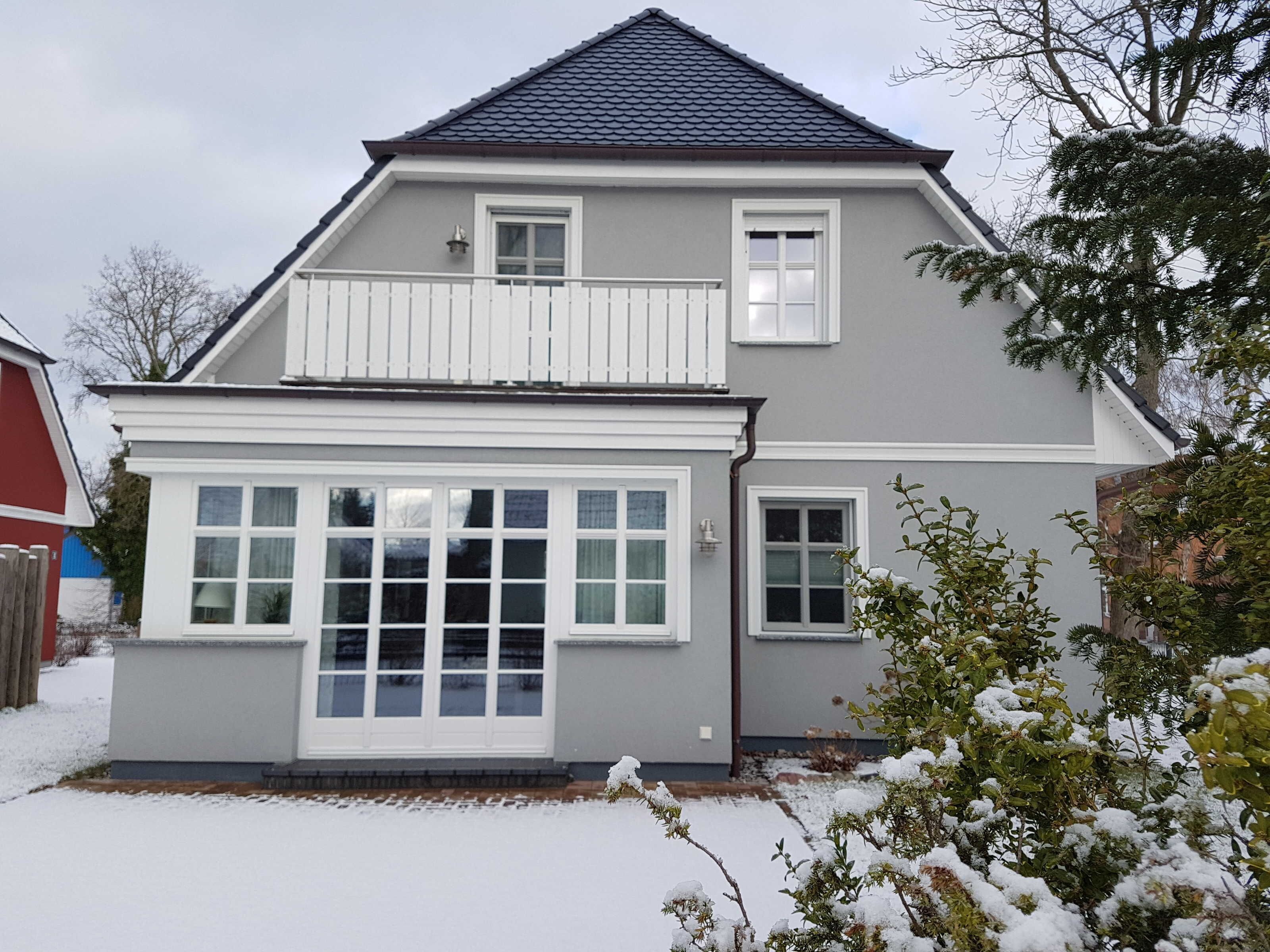 A two-story house with a balcony, large windows, and a snow-covered yard.