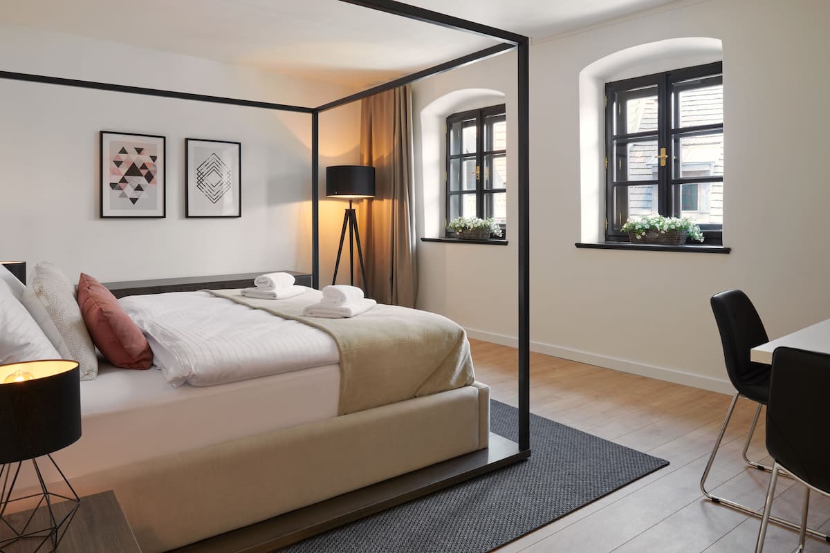 A modern hotel room with a four-poster bed, a desk, and a window with a view of the city.