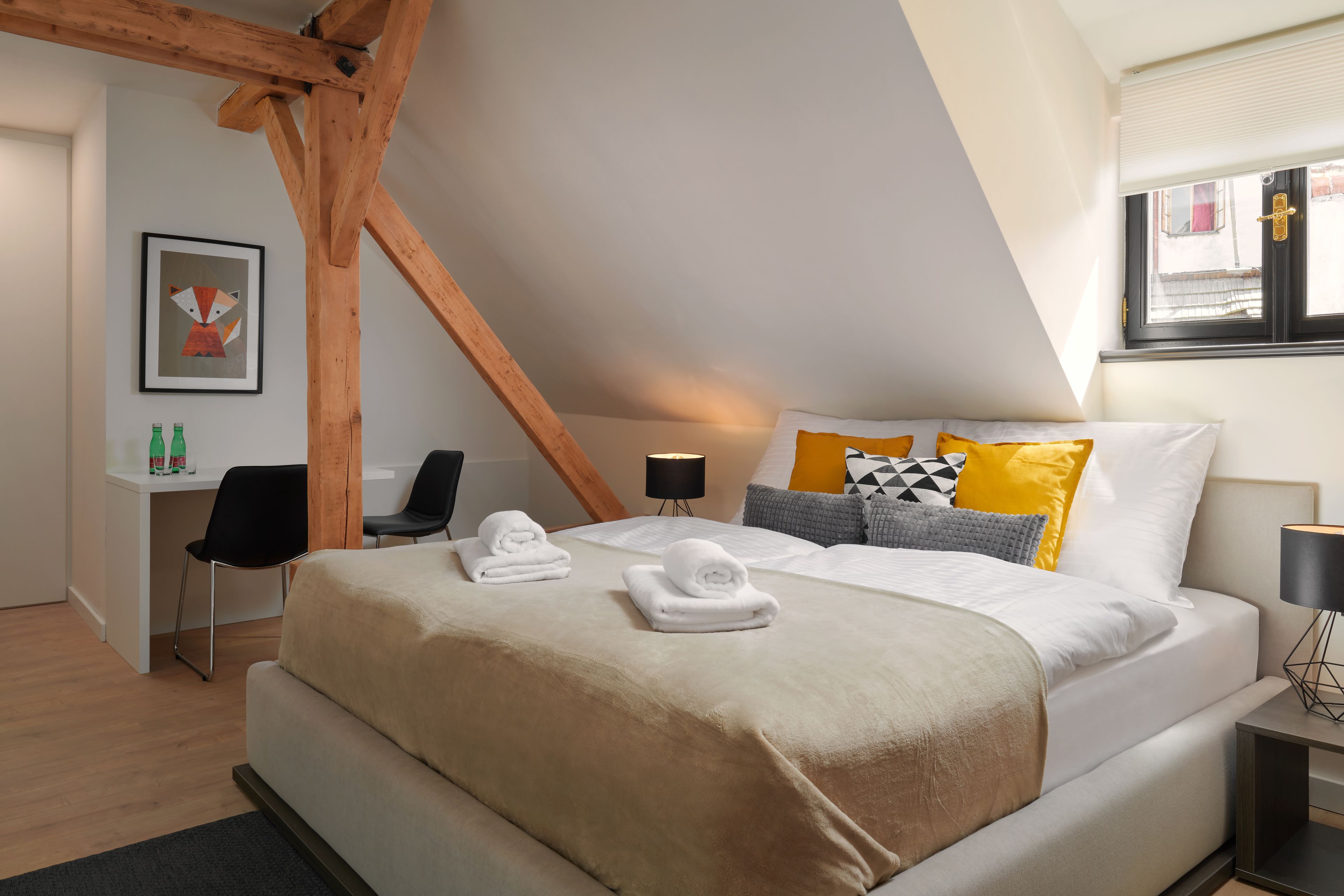 Habitación de hotel moderna con una cama grande, un escritorio y una silla. Hay toallas sobre la cama y un cuadro enmarcado en la pared.