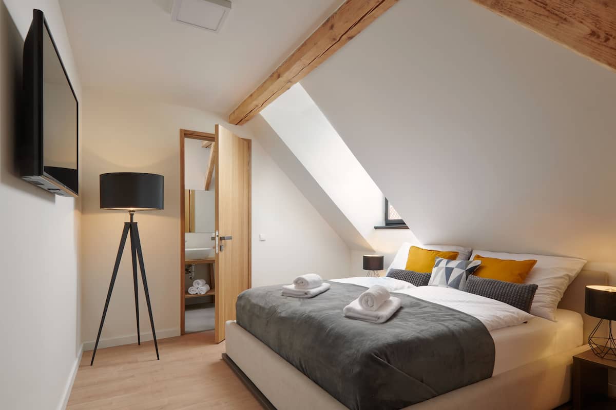A modern bedroom with a large bed, a standing lamp, and a flat-screen TV mounted on the wall.