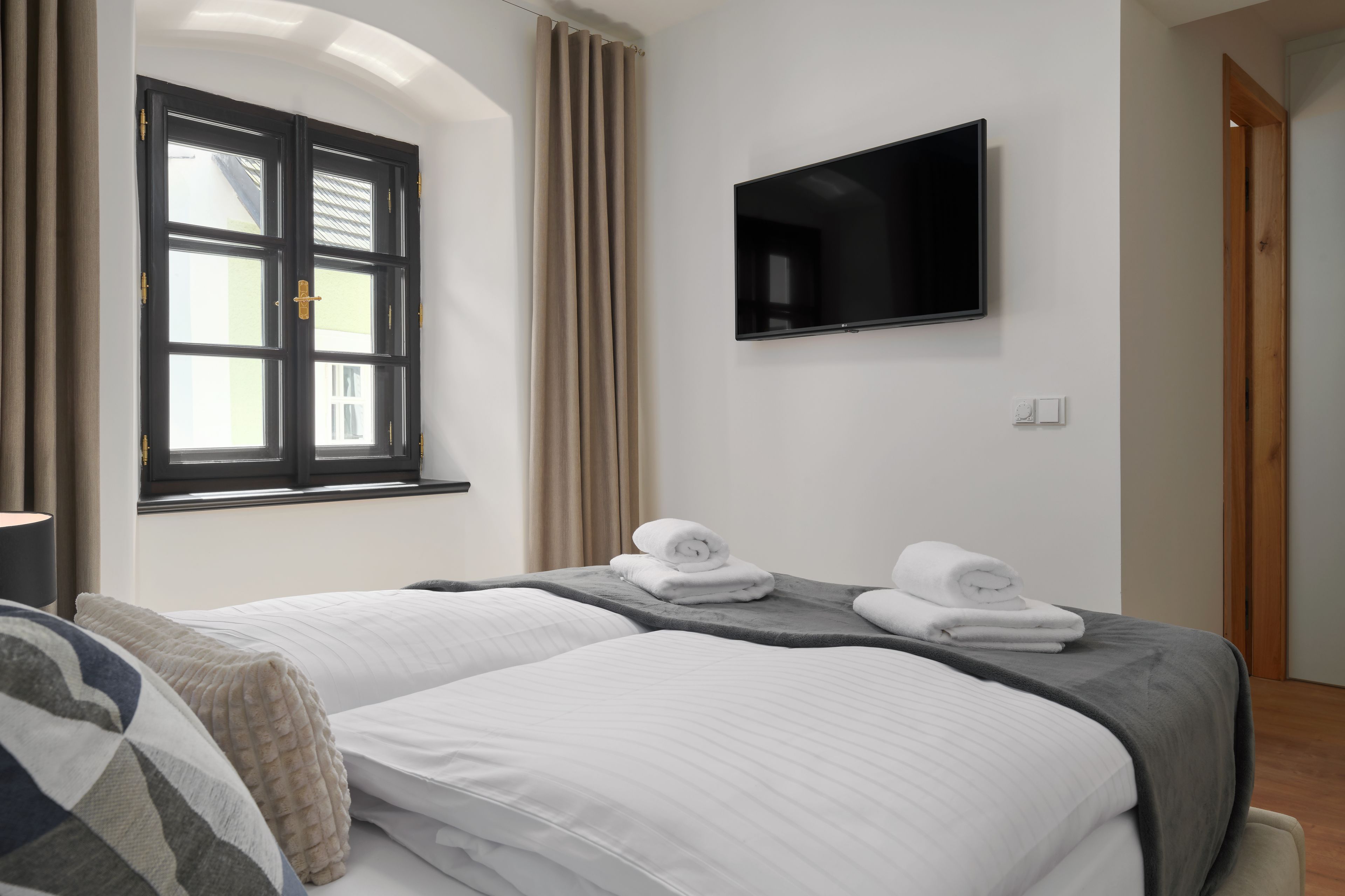 A hotel room with two beds, a flat-screen TV, and a window with curtains.