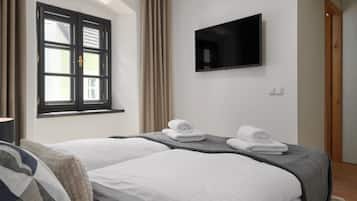 A hotel room with two beds, a flat-screen TV, and a window with curtains.